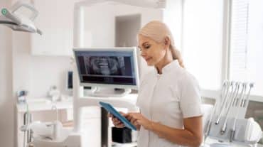 A female dentists looks at a tablet. Discover why solo orthodontic practices hit a growth ceiling and what successful doctors do differently to break through it.