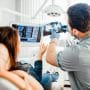 An orthodontists reviews an x-ray with a patient. Learn how DSOs and OSOs generate returns, where private equity fits in, and how doctor-owned models differ before you evaluate a partnership offer.