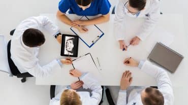 A group of orthodontists at a table together. Need help managing your orthodontic practice? Learn when to build your team, hire a consultant, or consider a partnership model.